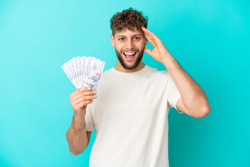 Poster - Young caucasian man taking a lot of money isolated on blue background with surprise expression