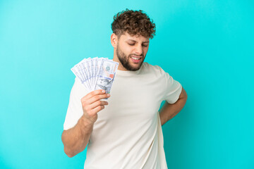 Poster - Young caucasian man taking a lot of money isolated on blue background suffering from backache for having made an effort