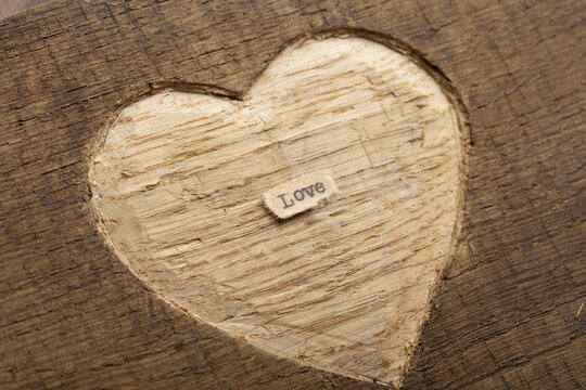 LOVE - tiny typed text note close up. Valentines Day greetings concept. Carved heart shape on wood as background for Valentines greeting card.