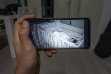 Unknown Man Holding Mobile Phone Checking Baby Monitor Watching His Child Sleeping Via Surveillance Camera At Night