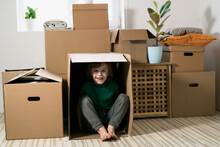 Boy Hiding In Inside A Huge Cardboard Box. He Is Playing And Looking Out Of A Box. Kid Is Happy About Moving Into A New Home.