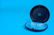 Black plastic case with transparent braces on blue background. Insivible removable retainers for orthodontic treatment