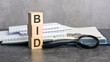 the word BID is written on wooden cubes on a gray background. close-up of wooden elements, magnifying glass, paper documents