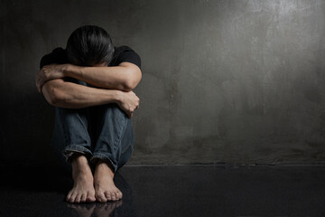 A man with depression sitting alone on the floor in the dark room