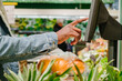 © wifesun - Stylish African-American guy in warm jacket with disposable mask weighs fresh oranges with digital scale in light supermarket