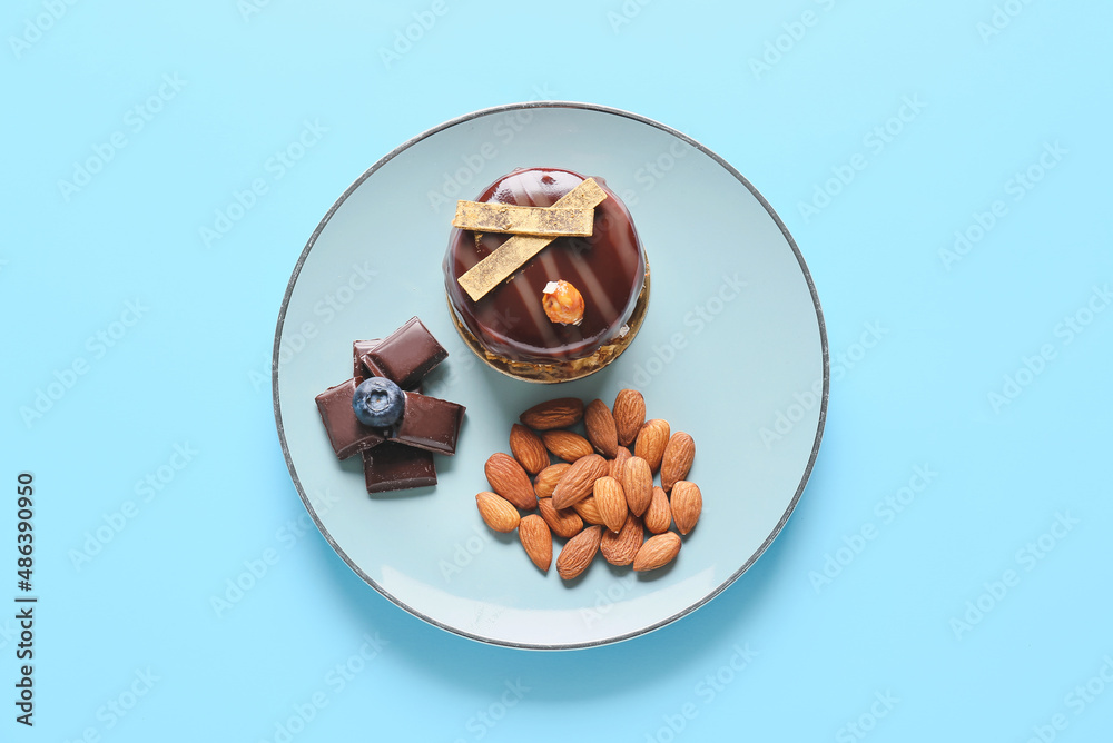 Plate with delicious cake, chocolate and almonds on blue background