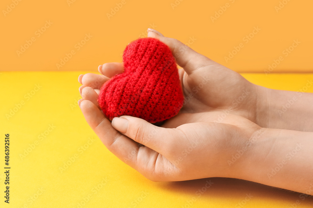 Female hands with knitted heart on color background, closeup. Donation concept