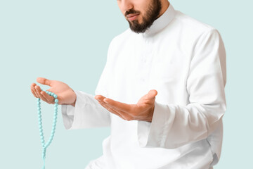 Wall Mural - Praying young Muslim man on light background