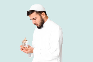 Wall Mural - Praying young Muslim man with fanous lamp on light background