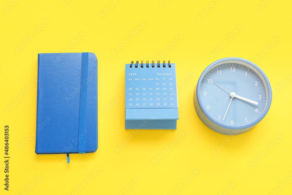 Notebook, calendar and alarm clock on yellow background