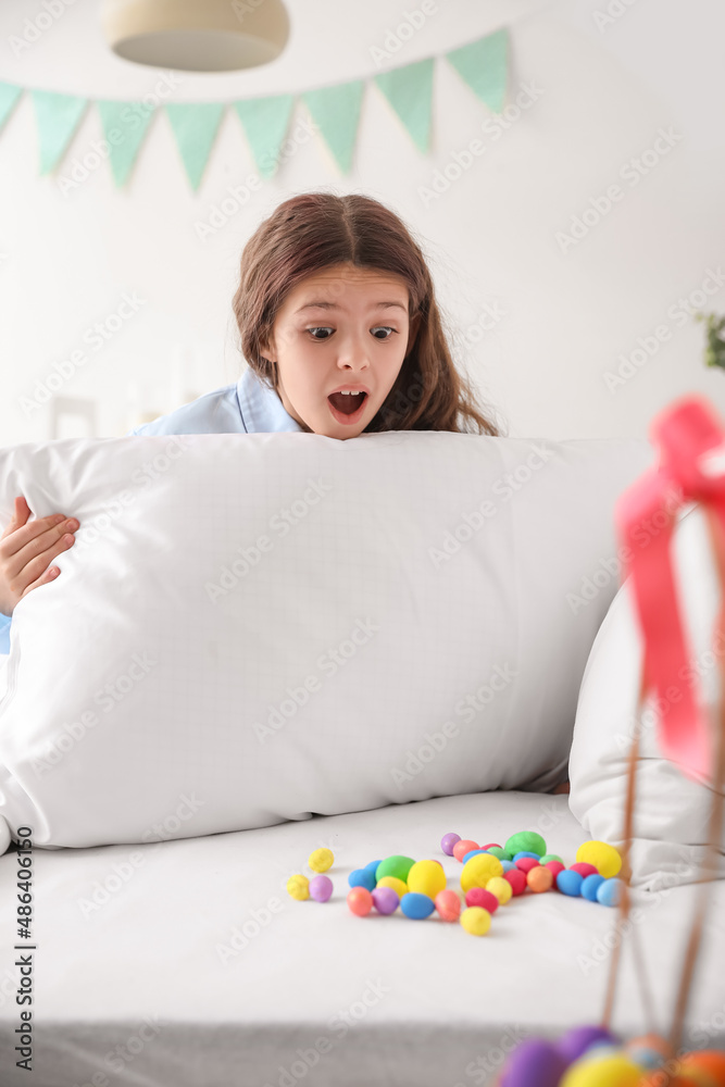 Cute little girl finds Easter eggs under pillow