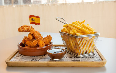 Sticker - A closeup of delicious french fries, nuggets with the Spanish flag, and a sauce on a wooden board