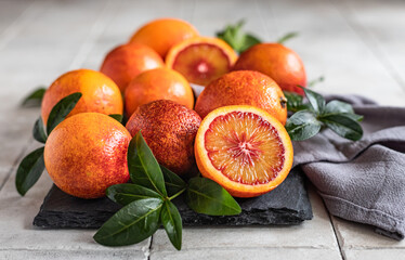 Wall Mural - Sliced and whole ripe juicy Sicilian blood oranges with leaves on black board, grey tiled background. Seasonal fruits.