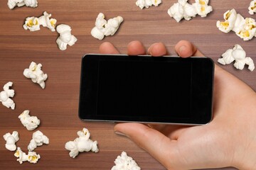 Sticker - Smartphone with blank screen and popcorn on the background. Streaming media and video-on-demand online