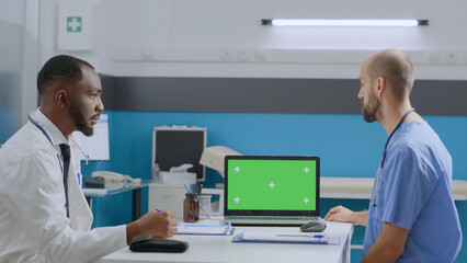 Wall Mural - Multi-ethnic team discussing medication treatment in front on mock up green screen chroma key laptop computer with isolated display. African american therapist doctor explaining medical expertise