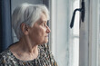 grey-haired sad upset elderly woman in her 60s looking out of the window medium close up indoor shot natural light. High quality photo