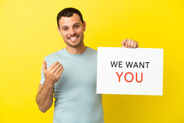 Brazilian man over isolated purple background holding We Want You board and doing coming gesture