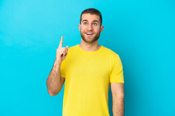 Poster - Young handsome caucasian man isolated on blue background thinking an idea pointing the finger up