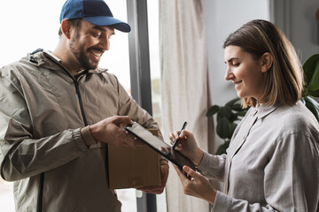 shipping, transportation and people concept - delivery man with parcel box and customer signing digital form in tablet pc computer at home