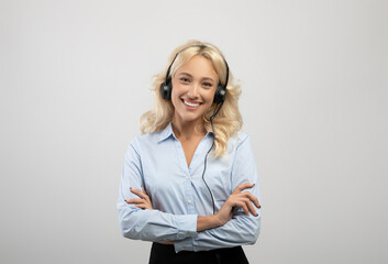 Portrait of happy caucasian call centre operator with headset crossing arms and smiling at camera, light background