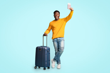 Wall Mural - Cheerful african american guy with suitcase showing flight tickets