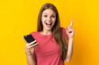 © luismolinero - Young woman using mobile phone isolated on yellow background pointing up a great idea