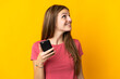 © luismolinero - Young woman using mobile phone isolated on yellow background looking up while smiling