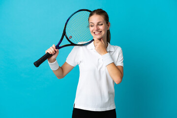 Wall Mural - Young woman tennis player isolated on blue background looking to the side and smiling