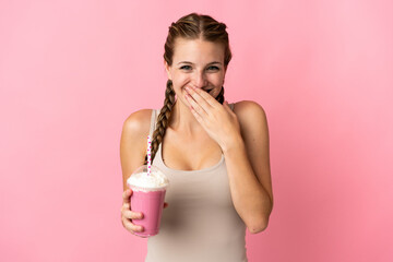 Young woman with strawberry milkshake isolated on pink background happy and smiling covering mouth with hand