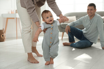 Wall Mural - Mother supporting her baby daughter while she learning to walk at home