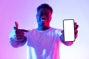 Poster - Handsome young black man pointing at smartphone with empty screen in neon light, selective focus. Mockup