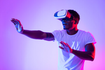 Poster - Excited African American guy in VR headset using virtual reality, touching imaginary screen in neon light