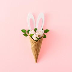 Wall Mural - creative layout made of bunny rabbit ears with flowers and ice cream cone on pastel pink background.