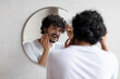 © Prostock-studio - Male beauty and haircare routine. Handsome indian man touching beard and hair, looking in mirror in bathroom