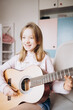 © Анна Молько - a cute little girl in a pink sweater is playing a baby guitar in her room. music training