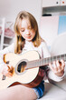 © Анна Молько - a cute little girl in a pink sweater is playing a baby guitar in her room. music training