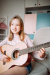 © Анна Молько - a cute little girl in a pink sweater is playing a baby guitar in her room. music training