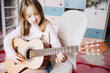 © Анна Молько - a cute little girl in a pink sweater is playing a baby guitar in her room. music training