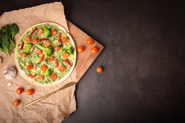 vegan pizza with broccoli and spinach pesto sauce, tomatoes on a dark table.