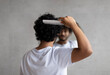 © Prostock-studio - Back view of indian curly man combing hair standing near mirror in bathroom. Male haircare routine concept