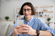 © Prostock-studio - Positive young man sitting on couch with smartphone, chatting with ladies, using dating mobile application on cellphone