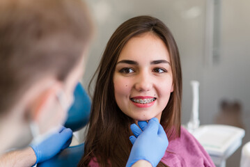 Close up of woman with brackets receiving dental braces treatment in clinic. Orthodontist using dental mirror and forceps while putting orthodontic braces on patient teeth. Concept of dentistry.