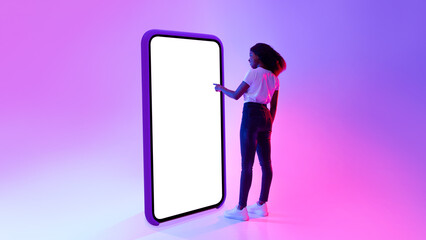 Wall Mural - Full length portrait of young black lady touching screen of huge cellphone in neon light, mockup for design