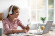 © Prostock-studio - Smiling pretty european teenager girl student in headphones watches video lesson at table in kitchen