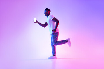 Poster - Excited young black guy with smartphone running in neon light, showing mockup for design on mobile device screen
