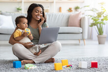 Remote Business. Happy Black Woman With Baby Working With Laptop And Cellphone