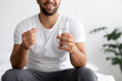 © Prostock-studio - Cropped smiling millennial muscular european male with glass of water and pill in white bedroom interior