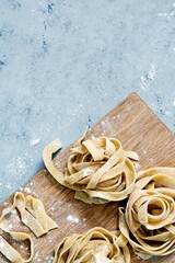 Raw yellow homemade italian pasta pappardelle, fettuccine or tagliatelle on a blue background, close up. Egg homemade noodles cooking process, long rolled macaroni, uncooked spaghetti .