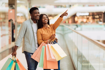 Wall Mural - Portrait of black couple with shopping bags pointing at window