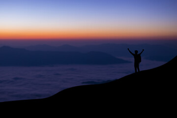 Wall Mural - Silhouette of young traveler and backpacker standing and open arm watched foggy landscape and mist alone on top of the mountain. He enjoyed traveling and was successful when he reached the summit.
